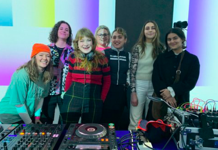 A group of people standing behind DJ decks.