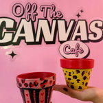 A hand is holding up a decorated pot in front of a  pink wall that has logo on it that reads 'OFF THE CANVAS'.