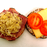 A bagel filled with pastrami, sauerkraut, cheese and tomato.