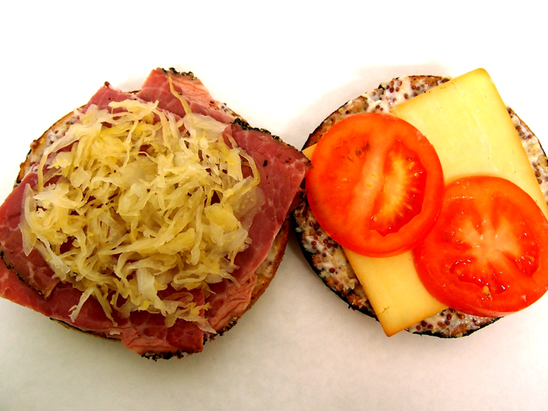 A bagel filled with pastrami, sauerkraut, cheese and tomato.