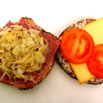 A bagel filled with pastrami, sauerkraut, cheese and tomato.