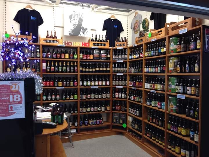 Wooden shop shelving filled with bottles and cans of all different types and brands of beer.