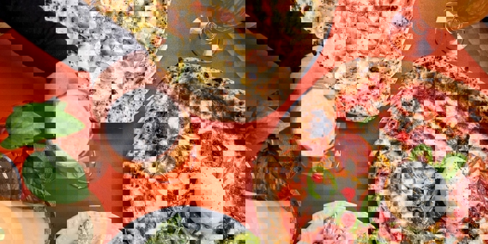 Two Neapolitan pizzas on a table, one topped with sausage and potatoes and the other with pepperoni and jalapeños, served with a Caesar salad and two glasses of beer.