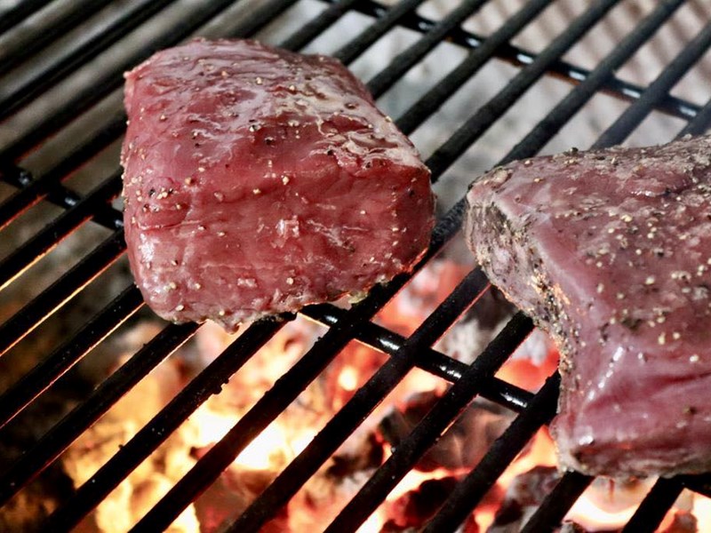 Two steaks on a charcoal grill.
