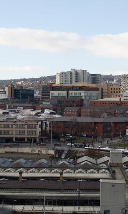 A hand holding a pint of beer up to the skyline of Sheffield from behind the train station