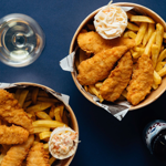 An overhead shot of two bowls of breaded chicken and chips and a bottle of beer.