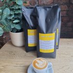 A cup of coffee on a table, along side some bags of coffee beans,  at Made by Jonty.