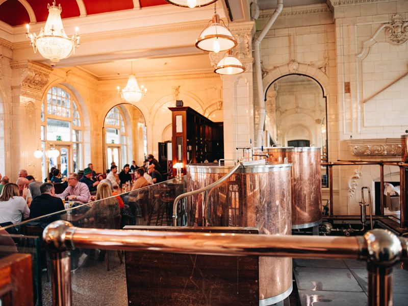 Sheffield Tap copper beer tanks to the right, with groups of people sat down talking and drinking to the left.
