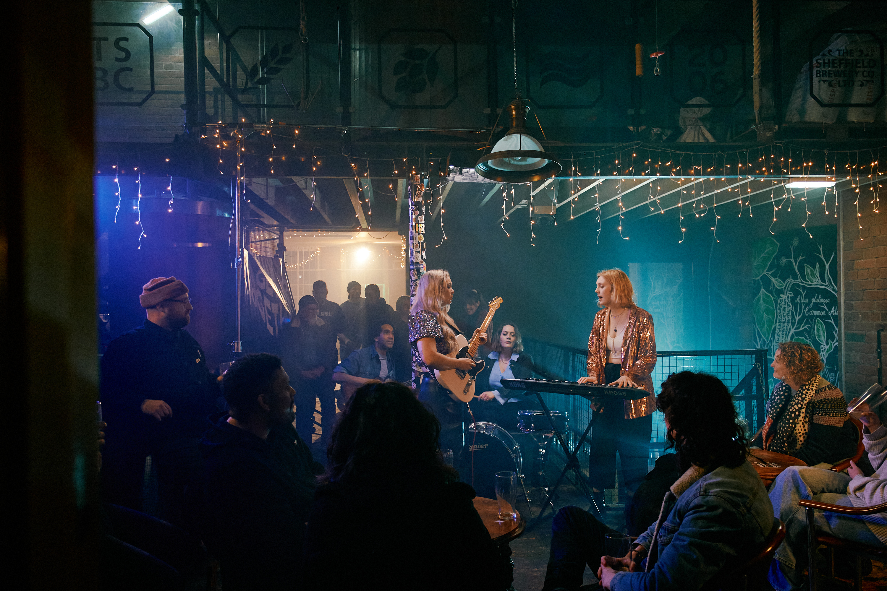 A three piece band plays live at Alder, in front of a crowd who are drinking and having a great time.