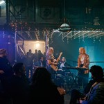 A three piece band plays live at Alder, in front of a crowd who are drinking and having a great time.