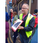 A tour guide talks to a group of people on a tour in Sheffield, whilst holding up an illustration. 