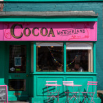 Front view of the Cocoa Wonderland shop with pink and teal signage and a decorated window display.