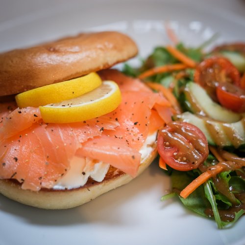 A bagel on a plate, filled with salmon and cream cheese and a side salad.