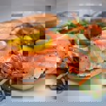 A bagel on a plate, filled with salmon and cream cheese and a side salad.