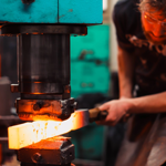 A man shaping a piece of white-hot metal in a huge press.