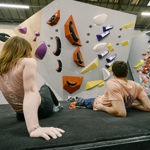 Two people are lying on the floor having a rest at an indoor climbing centre.