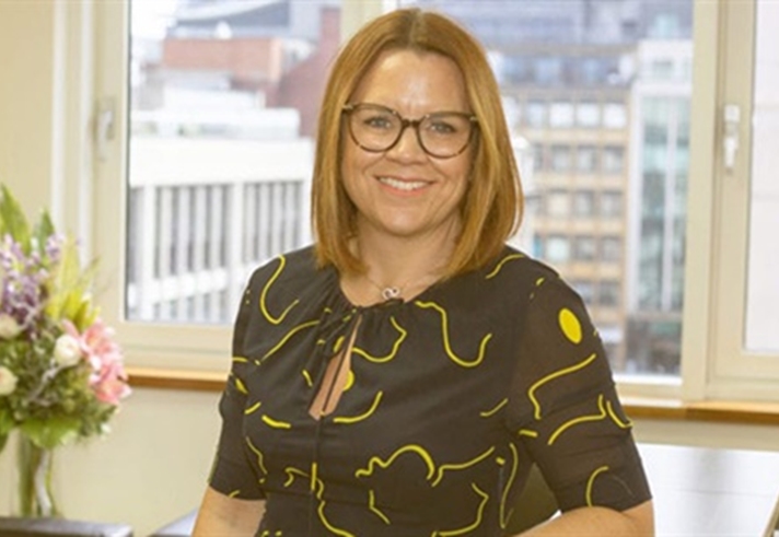 A woman stands amiling atthe camera in an office.