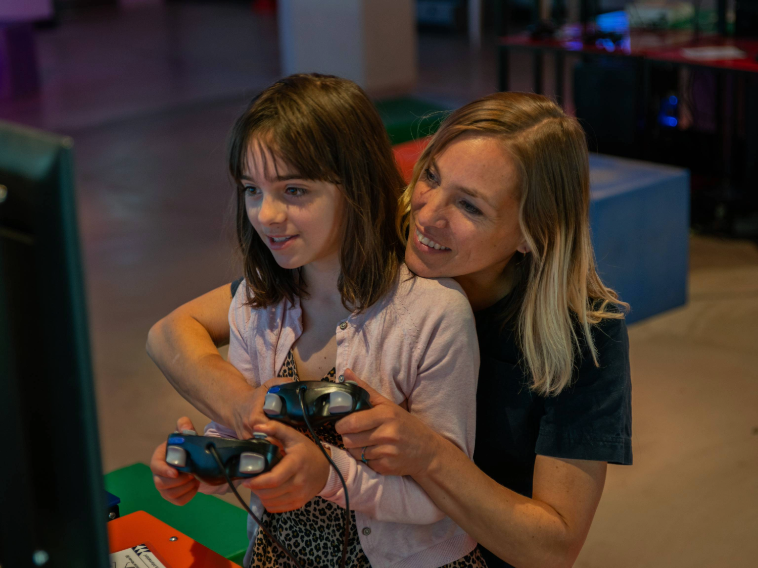 A person with a child sat on their knee are playing a video game together. In the background are displays of video games from the history of the video game industry.
