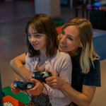 A person with a child sat on their knee are playing a video game together. In the background are displays of video games from the history of the video game industry.