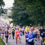 Group of people running in Sheffield Half Marathon, in leafy surroundings of the city. There are tall trees either side of the road they are running along.