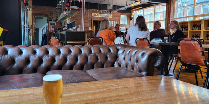 Inside at Perch Brewhouse, a pint of beer stands on a wooden table. Behind the table is a leather sofa.