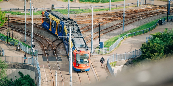 A Sheffield Supertram travelling along curved tracks, seen from above, with rail lines, walkways and greenery surrounding the junction.