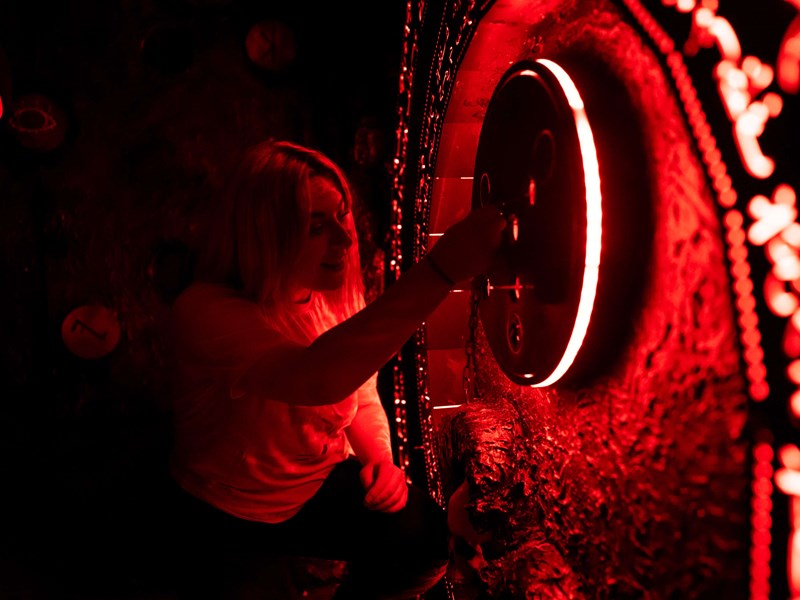 A woman trying to solve a puzzle in a dimly lit room at The Great Escape Game.