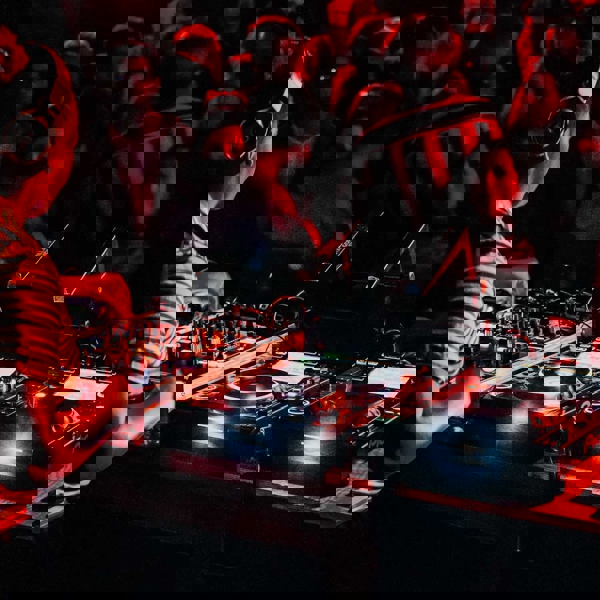 A female DJ of African heritage is mixing at the decks, for a nightclub crowd.