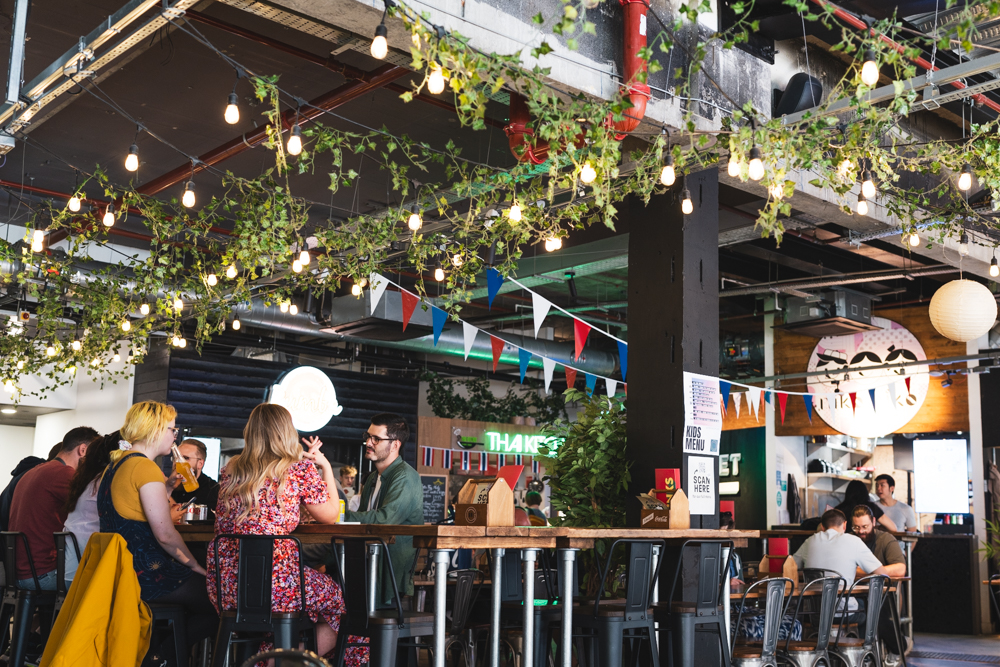 Inside the foodhall Sheffield Plate. Lots of people are sat at table eating and drinking.