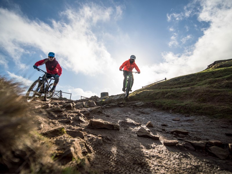Two people mountain biking down a slope out in the countryside.