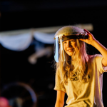 A person, in a dark environment, is smiling. They are wearing protective head gear with a visor.