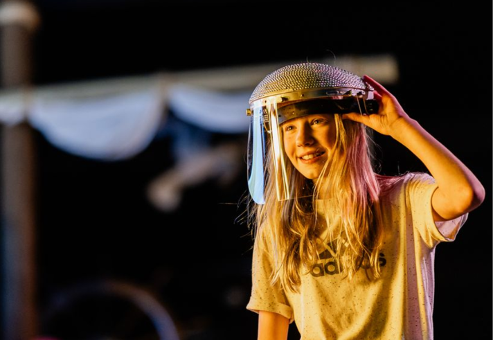 A person, in a dark environment, is smiling. They are wearing protective head gear with a visor.