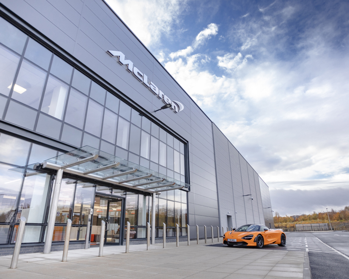 An orange McLaren car parked outside the glass McLaren building at The Advanced Manufacturing Innovation District.
