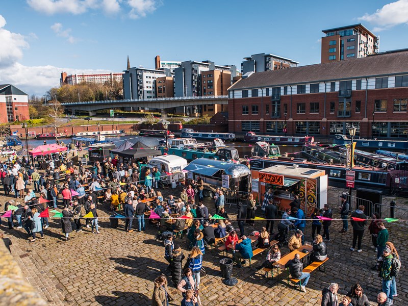 Quayside Market At Victoria Quays in full flow with people wandering about, in bright sunshine, and sitting at trestle tables eating.