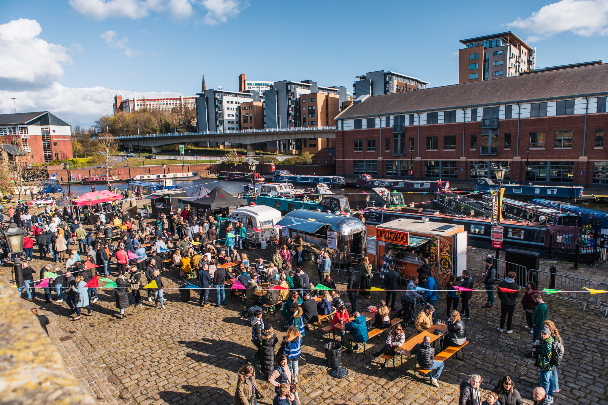 Quayside Market At Victoria Quays in full flow with people wandering about, in bright sunshine, and sitting at trestle tables eating.