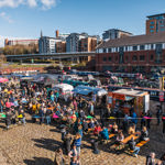Quayside Market At Victoria Quays in full flow with people wandering about, in bright sunshine, and sitting at trestle tables eating.