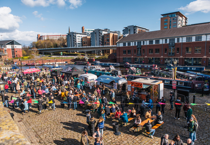 Quayside Market At Victoria Quays in full flow with people wandering about, in bright sunshine, and sitting at trestle tables eating.