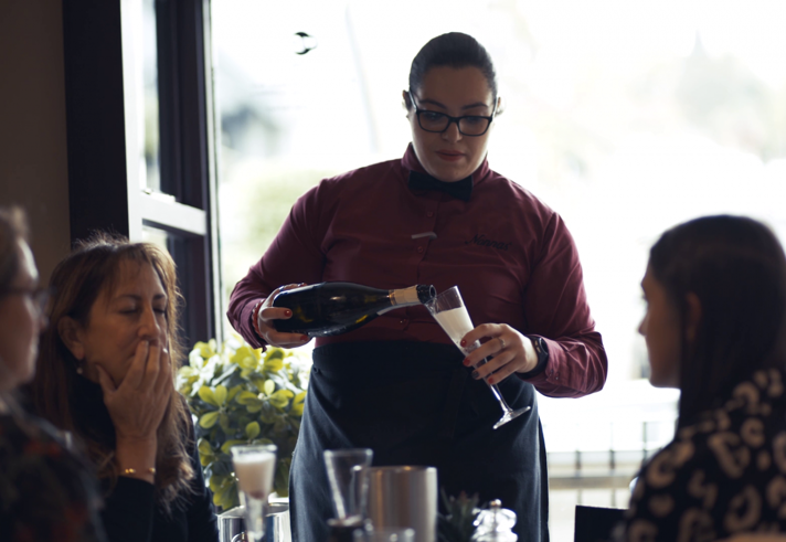 A member of staff pours sparkling wine for a table of guests at Nonnas Restaurant.