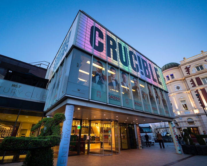 The exterior of the Crucible Theatre, lit up in the dusk with colourful light.
