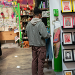A person looking at a display of prints at a stall in an indoor market.