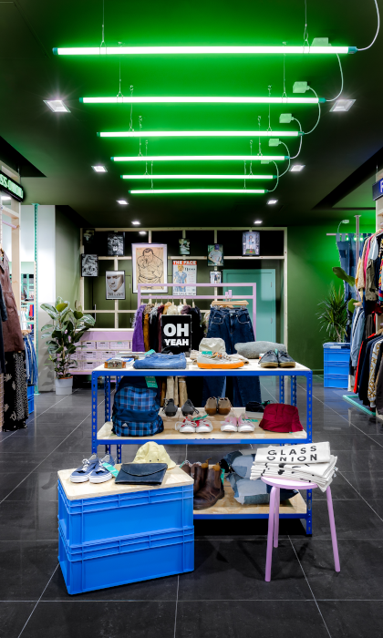 Inside the Glass Onion shop. All the walls are full of clothes on rails. In the centre of the shop are tables with accessories on display.