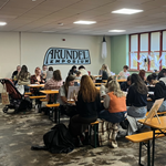 A communal area with tables and benches, full of people.