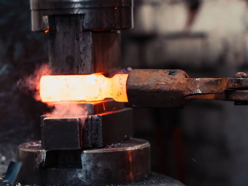 A piece of white-hot metal being shaped in a huge hammer press.
