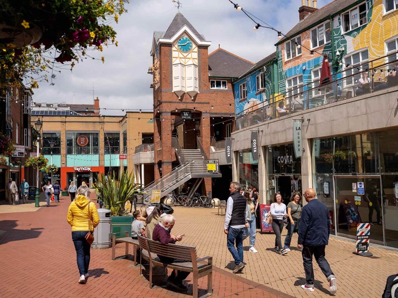 Lots of people are walking about in Orchard Square on a sunny day.