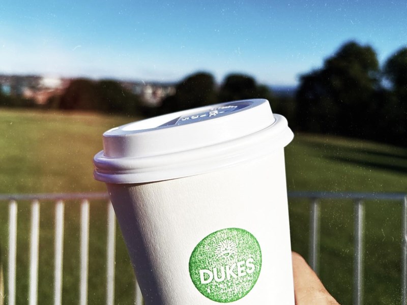 Dukes in the Park branded paper cup with the park in the background
