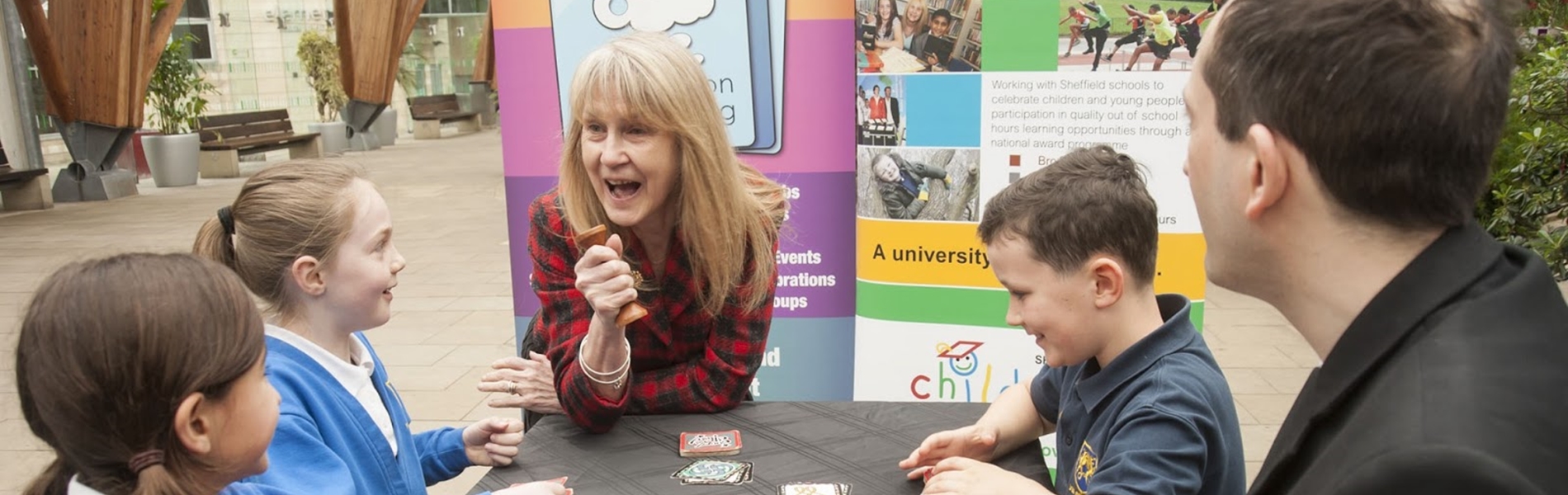 Three children and two adults are sat at a table in Sheffield Winter Garden, playing a game.