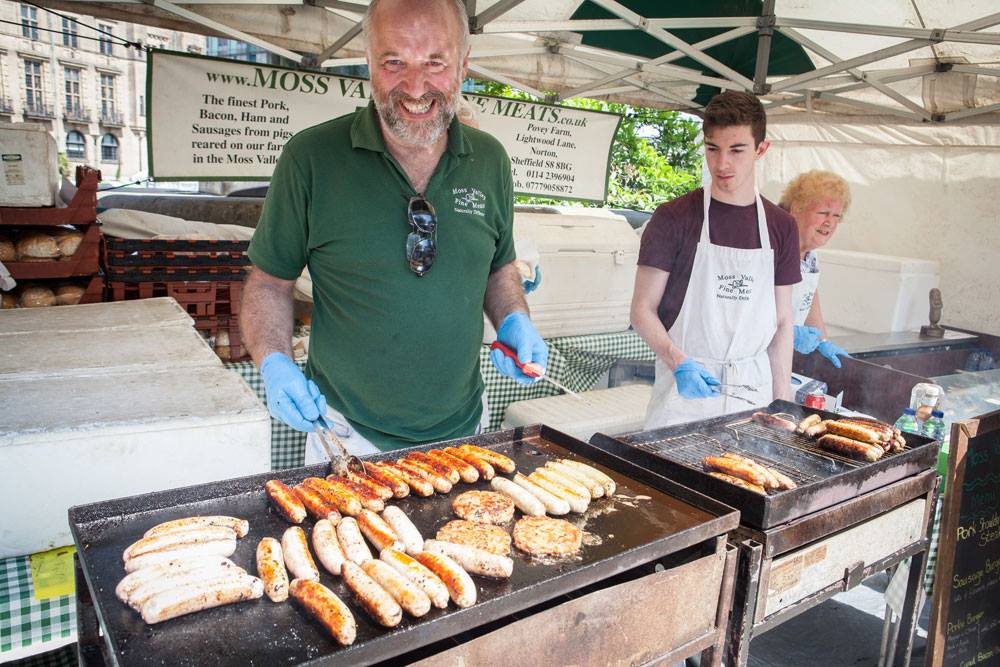 A street food trader turns an array of meat items sizzling on a BBQ