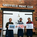 Three people standing outside Sheffield Print Club holding prints they have made.