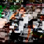 A man sings into a microphone in front of a crowd. Behind him is a man mixing on two DJ decks.