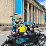 A group of people in cycling gear posing outside The City Hall with the Sheffield Cycle Tours bikes.